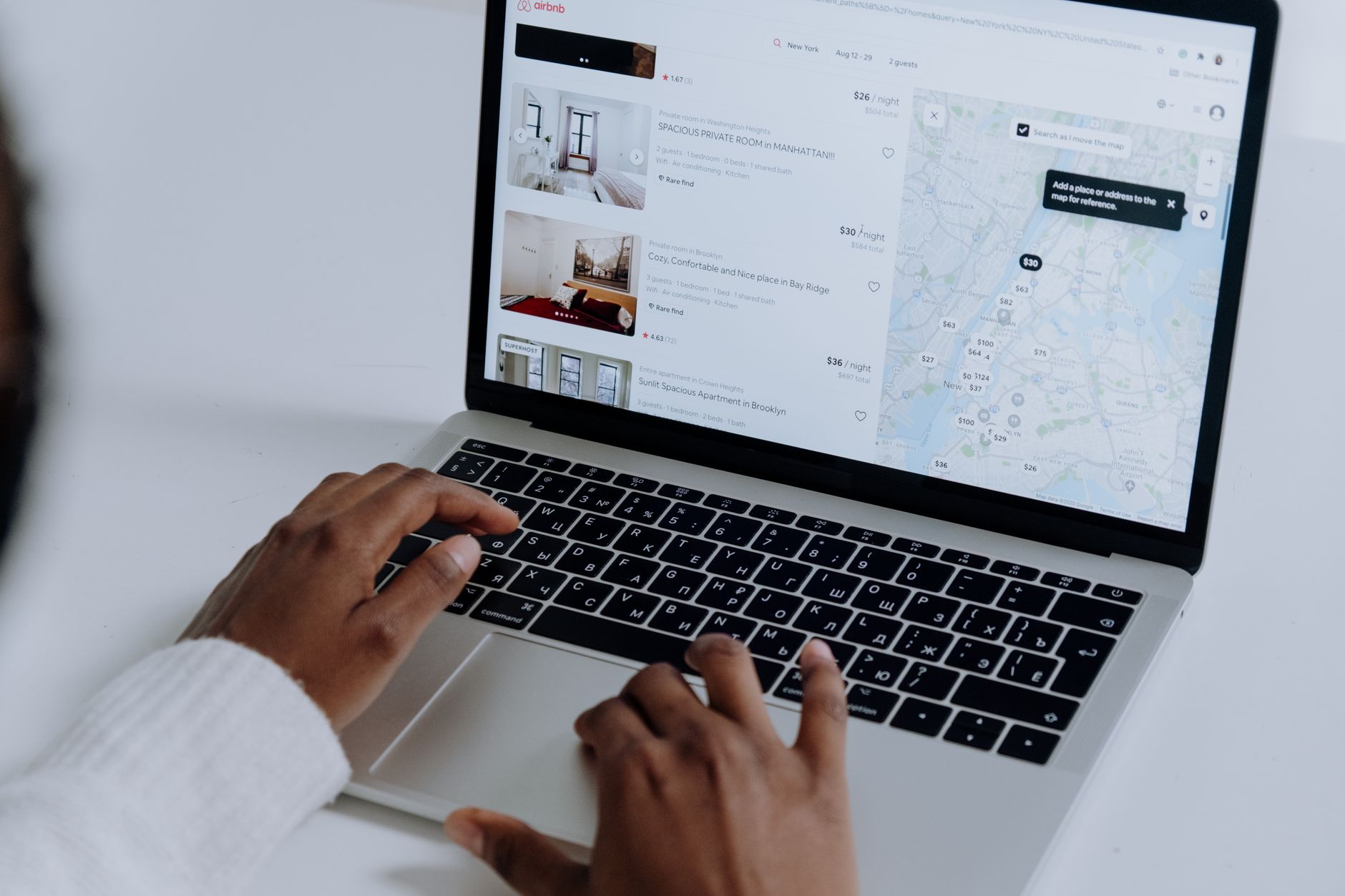 Person's hands typing on laptop displaying Airbnb rental listings and map for New York accommodation search