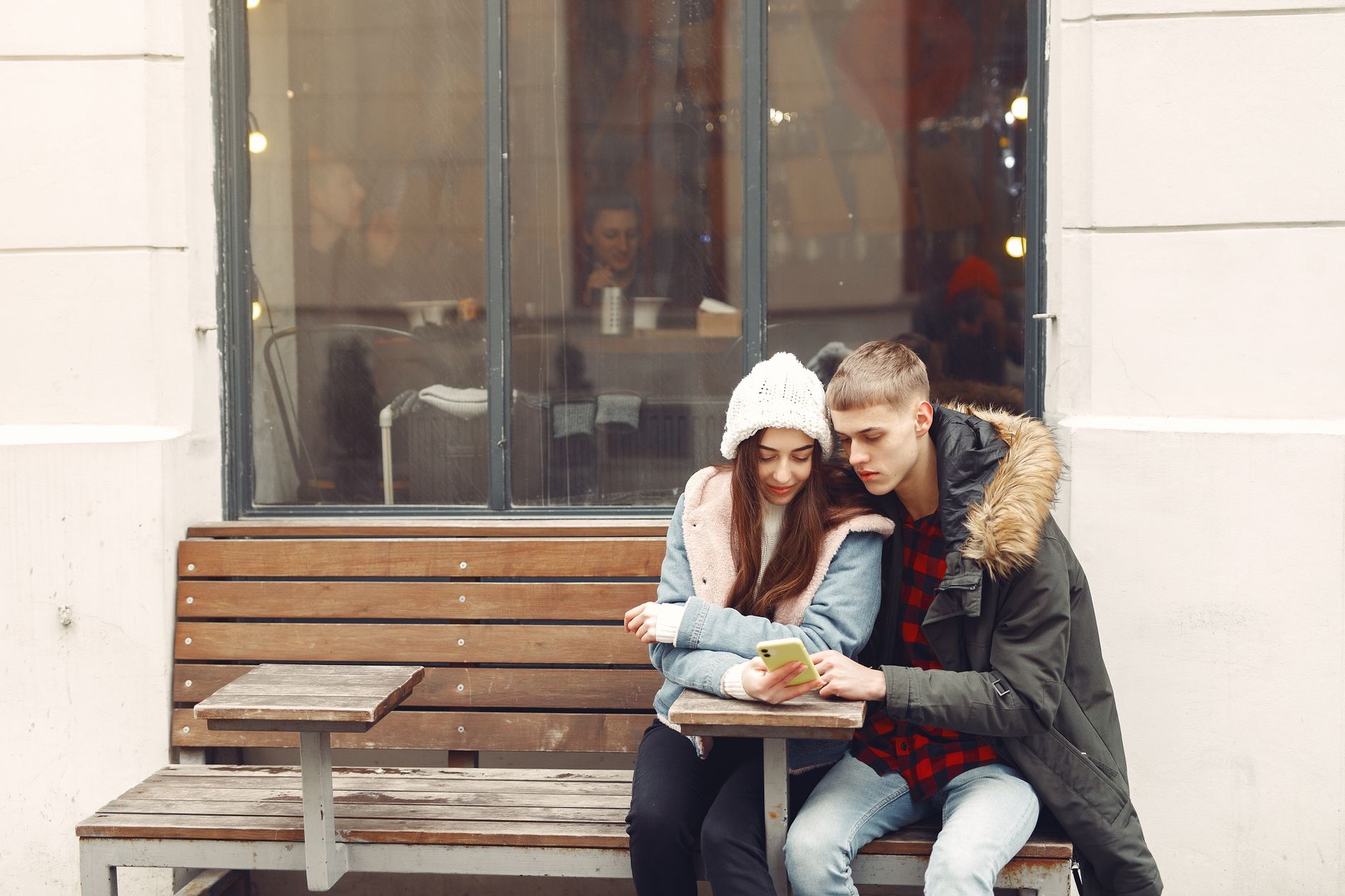 Two teenagers sitting on a bench outdoors looking at a smartphone together